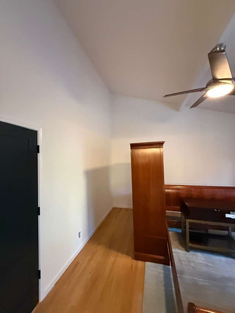 Vaulted-ceiling room repaint with black interior door and warm hardwood floors